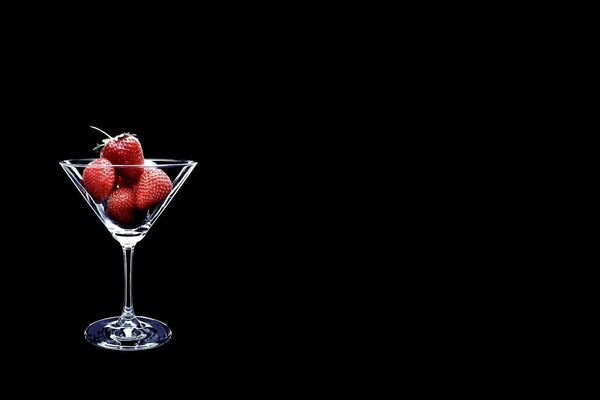 Erdbeeren in einem Martini-Glas. Schwarzer Hintergrund. Minimal art