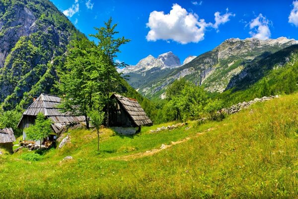 Cabanes dans les montagnes vertes sous un ciel bleu ouvert avec des nuages