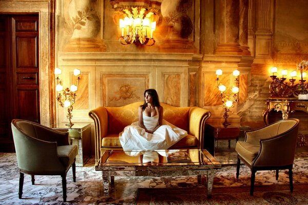 Brunette assise sur le canapé dans le château entouré de luminaires