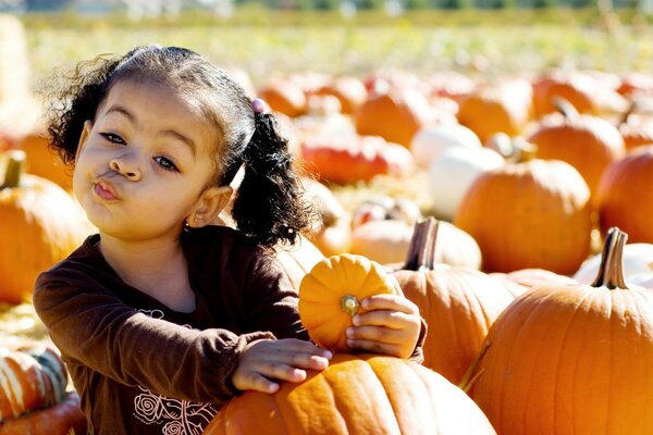 El niño que se sienta en las calabazas y sostiene también la calabaza en la mano