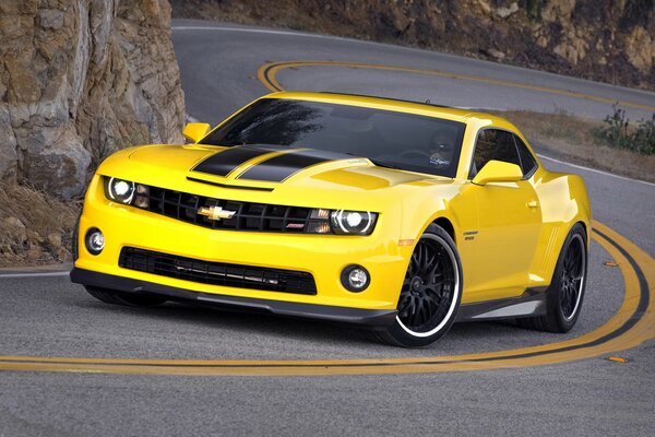 A yellow Chevrolet with black stripes is driving on the road