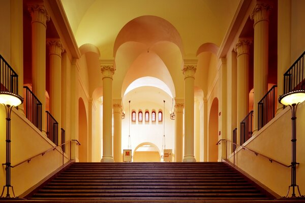 A wide staircase inside the building with beautiful architecture in warm yellow tones