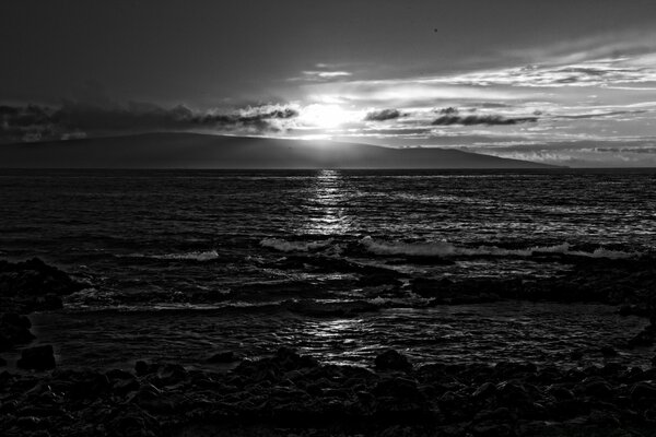 Foto en blanco y negro del agua del mar desde la playa en el fondo de la puesta de sol