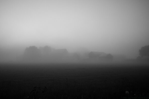 Black and white photo of a field of village houses in the fog