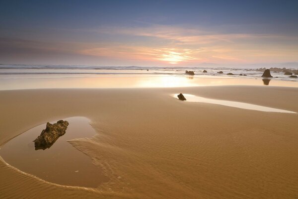 Sandstrand mit Steinen bei Sonnenuntergang