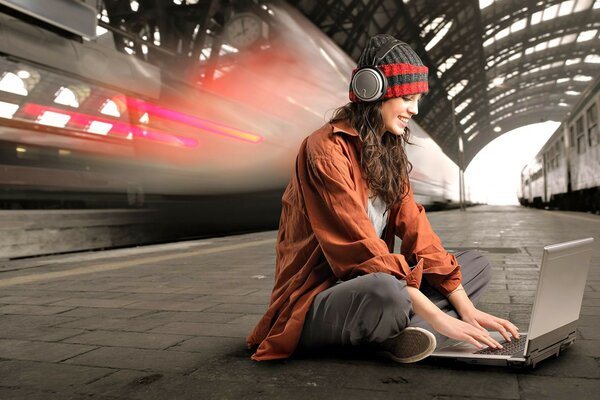 A girl with headphones is sitting at her laptop