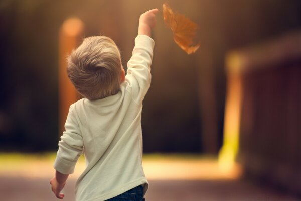 Blonder Junge schickt ein Blatt zum Fliegen