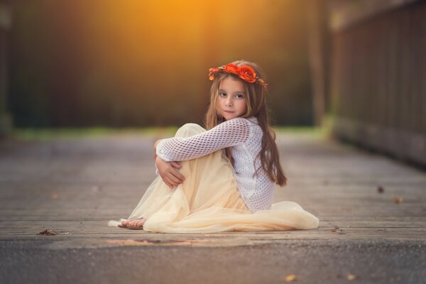 A little girl on the floor with a wreath of red flowers