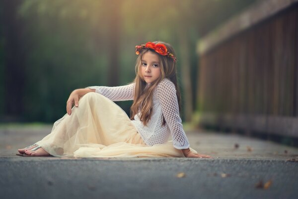 A girl in a wreath is sitting on the asphalt