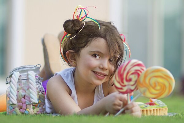 A smiling girl is lying on the grass and holding sweets in her hands