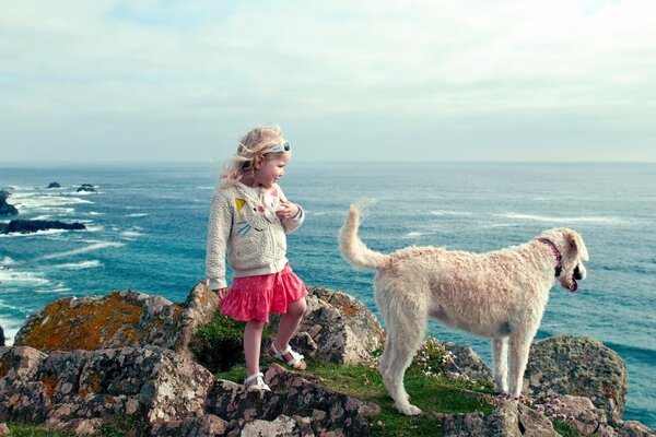 Menina em uma saia vermelha na beira de um penhasco com um cachorro