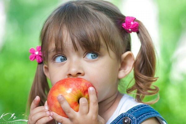 A little girl eats a ripe apple