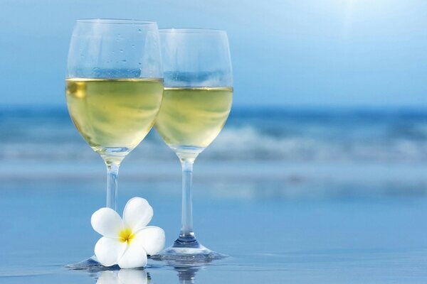 Two wine glasses with a drink and a flower on a blurred background of the sea