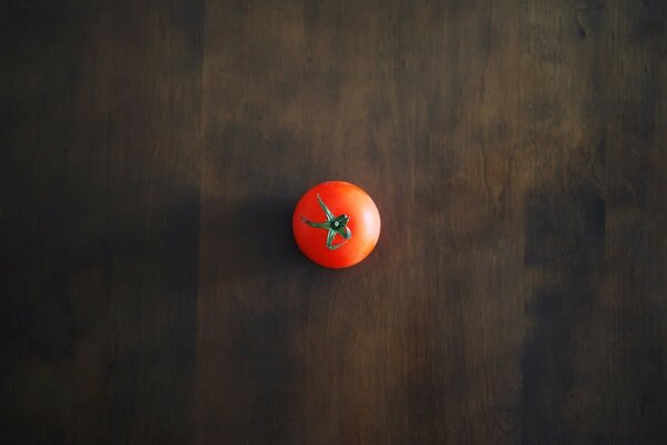 Un tomate rojo descansa sobre un piso de madera oscura