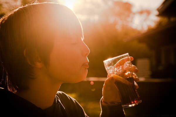 Un niño con los ojos cerrados de placer . beber una bebida de un vaso