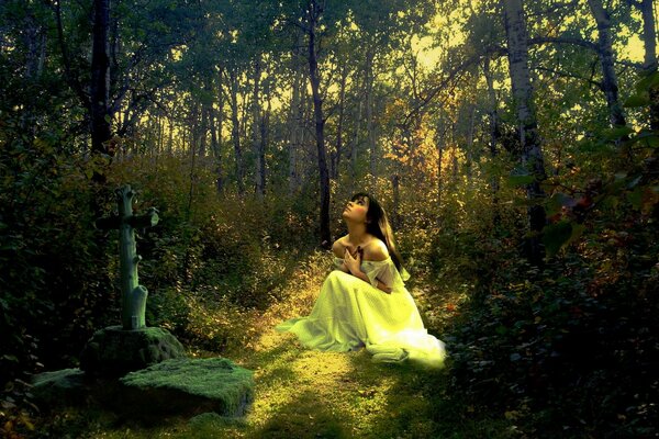 A young girl in a white dress prays alone in front of a crucifix in a forest clearing