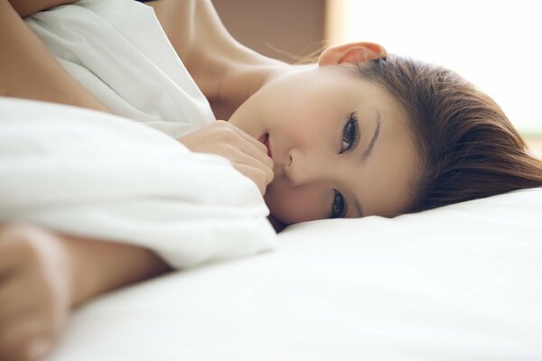 Chica asiática en ropa de cama blanca como la nieve