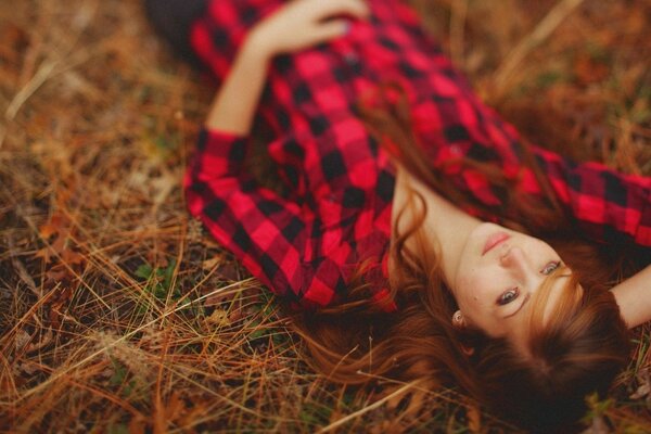 A girl in a tattered shirt is lying on dry grass