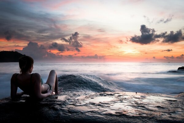 A girl on the seashore looks at the sunset