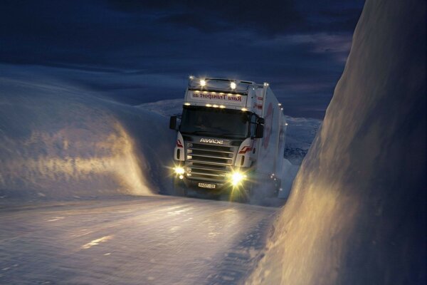 Un camión que conduce cuesta arriba en una pista cubierta de nieve de invierno por la noche