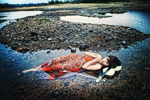 The musician girl is lying in a shallow pond