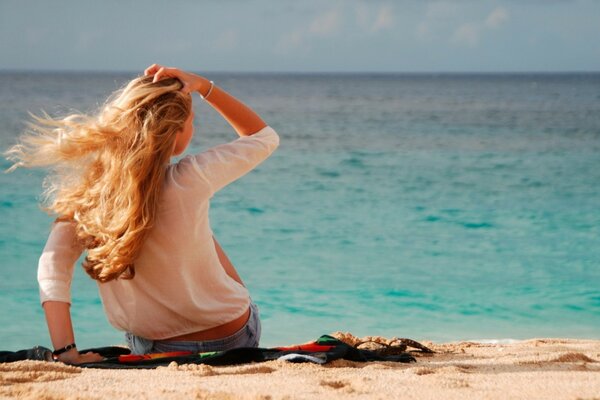 Ragazza con i capelli lunghi si siede sulla riva del mare