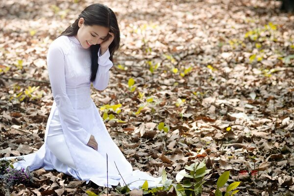 A girl in white is sitting on autumn leaves