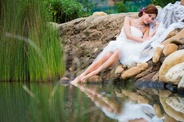 Una donna in abito bianco giace vicino a uno stagno