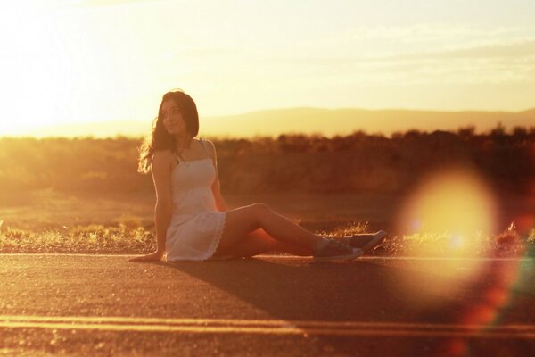 Jeune fille assise sur la route sur fond de coucher de soleil