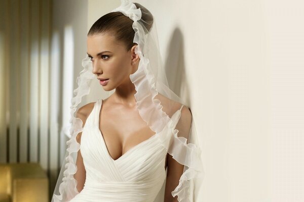 The bride in white is standing against the wall