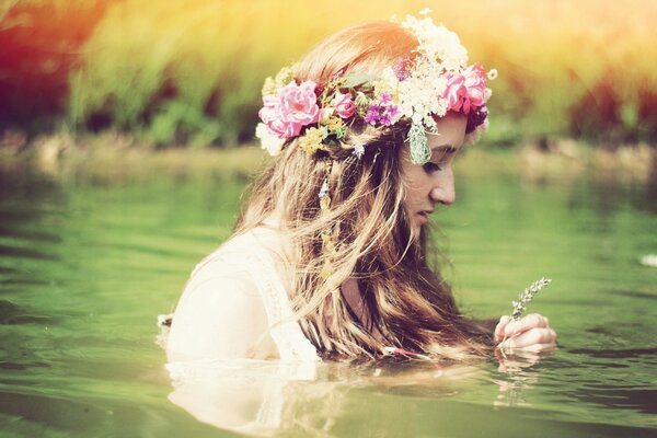 Beautiful blonde girl in the water with a wreath