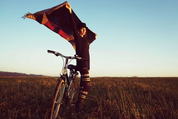 Ragazza con una bicicletta che tiene un fazzoletto sopra la testa al vento