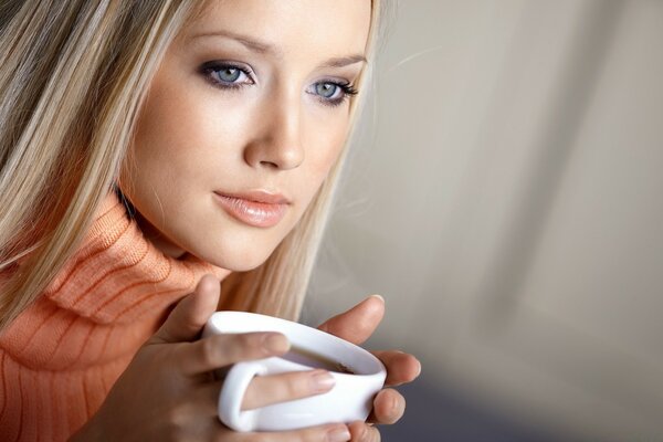 Mädchen mit einer Tasse Kaffee. Hübsches Gesicht. Blonde. Wärme aus einer Tasse Kaffee