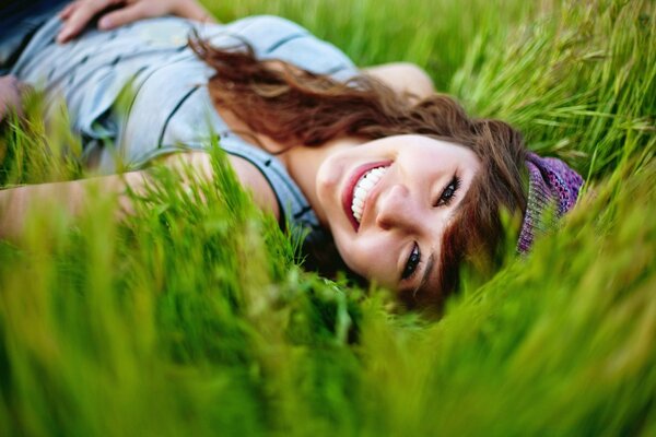 Mädchen mit langen Haaren liegt und lächelt im grünen Gras