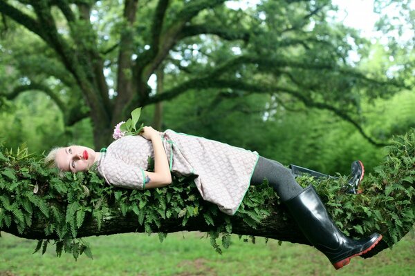 The girl is lying on a green tree branch