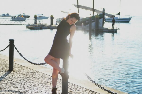 A girl in a short dress on the pier leans on a metal post