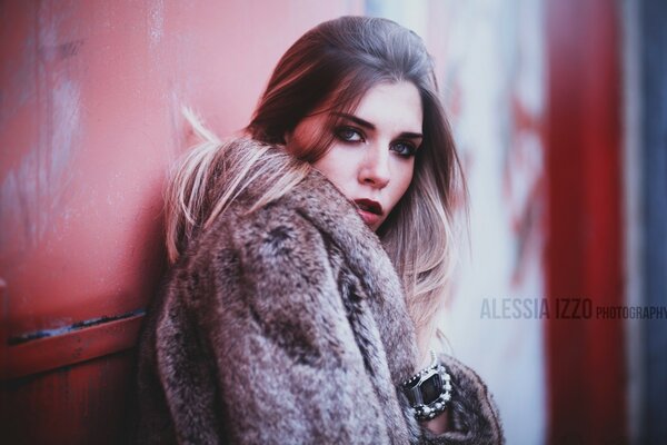 Portrait of a girl in a fur coat against the wall