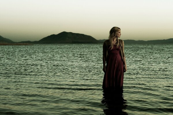 Chica junto al mar en el fondo de la puesta de sol y las montañas