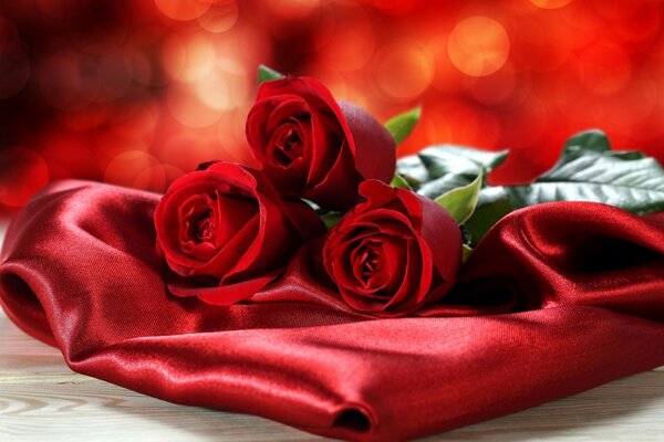 Three red roses lie on red silk