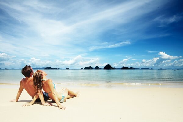 Chico con chica en la playa junto al mar mirando el cielo azul