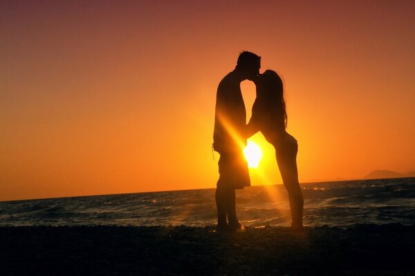 Kissing couple on the background of sunset by the sea