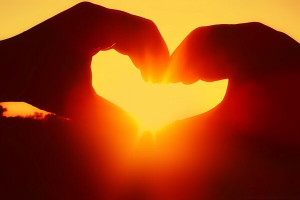 The hands are folded in a heart through which the sun can be seen