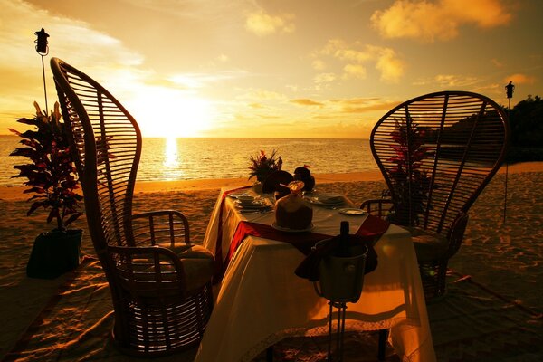 Mesa e cadeiras no fundo da praia e do pôr do sol