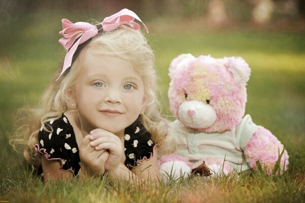 A girl with a bow is lying with a teddy bear