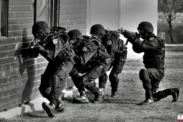 A group of soldiers in special equipment sneak near the wall of the building