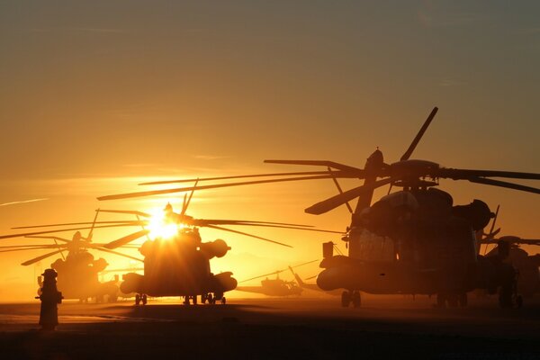 Um grupo de helicópteros militares em um campo de decolagem em meio ao pôr do sol