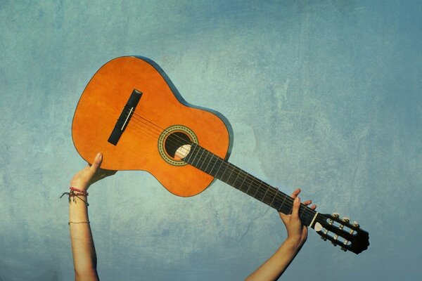 Gitarre in den Händen eines Mannes über dem Kopf auf blauem Hintergrund