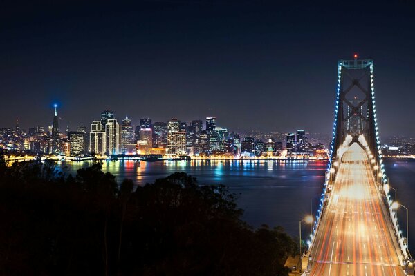 A city sparkling with lights of all colors on the horizon, a grandiose bridge in the foreground