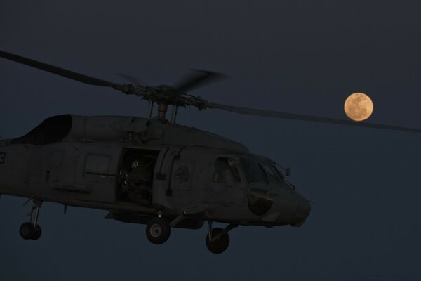 A helicopter is flying against the background of a full moon