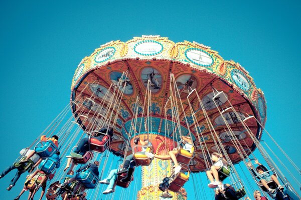 People riding on a carousel with suspended seats on a blue sky background